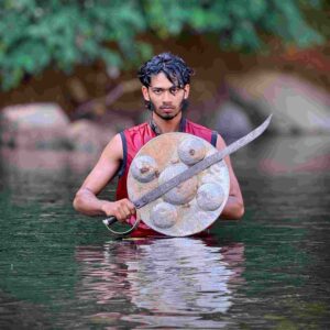 Kalaripayattu practitioner holding traditional sword and shield standing in a river in Wayanad