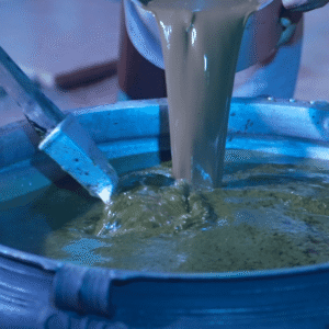 Close-up of the traditional artisanal brewing process of Mukkoottu Thailam, with thick, herbal-infused oil being poured into a large traditional vessel for Kalaripayattu oil therapy.